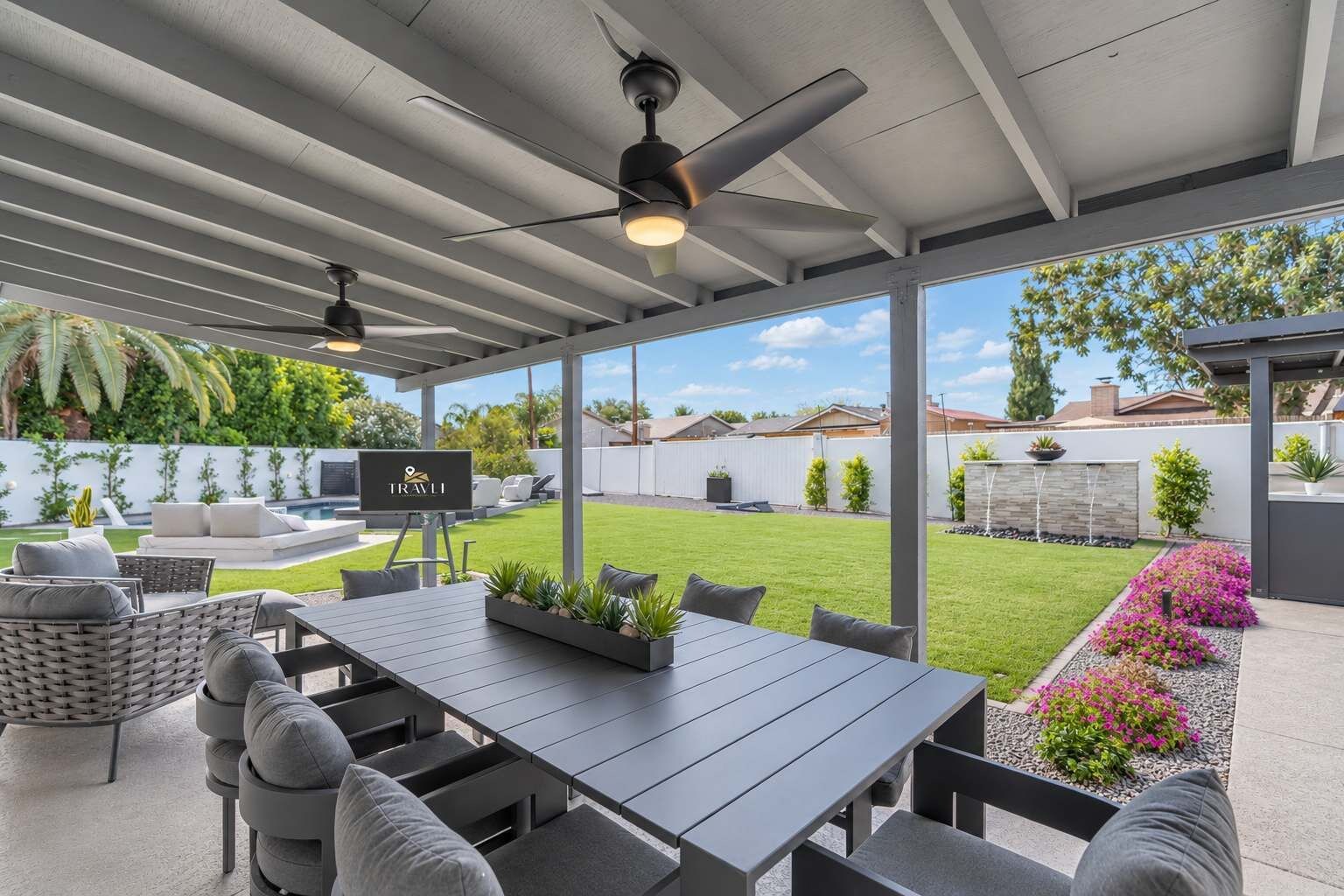 Een buitenpatio met een tafel, stoelen, een plafondventilator en een televisiescherm.