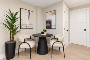 Een kamer met een ronde tafel, twee stoelen, een potplant en twee abstracte schilderijen aan de muur.