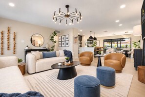 A modern living room with a sofa, armchairs, ottomans, a coffee table, and a chandelier. - NEW | The Barrington | Old Town Designer Retreat (Scottsdale)