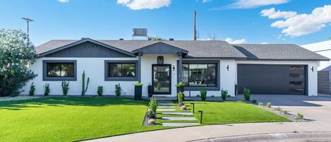 A modern two-story house with a well-maintained lawn, a driveway leading to the garage, and a clear blue sky.