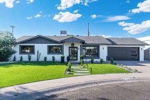 A modern two-story house with a well-maintained lawn, a driveway leading to the garage, and a clear blue sky. - NEW | The Barrington | Old Town Designer Retreat (Scottsdale)