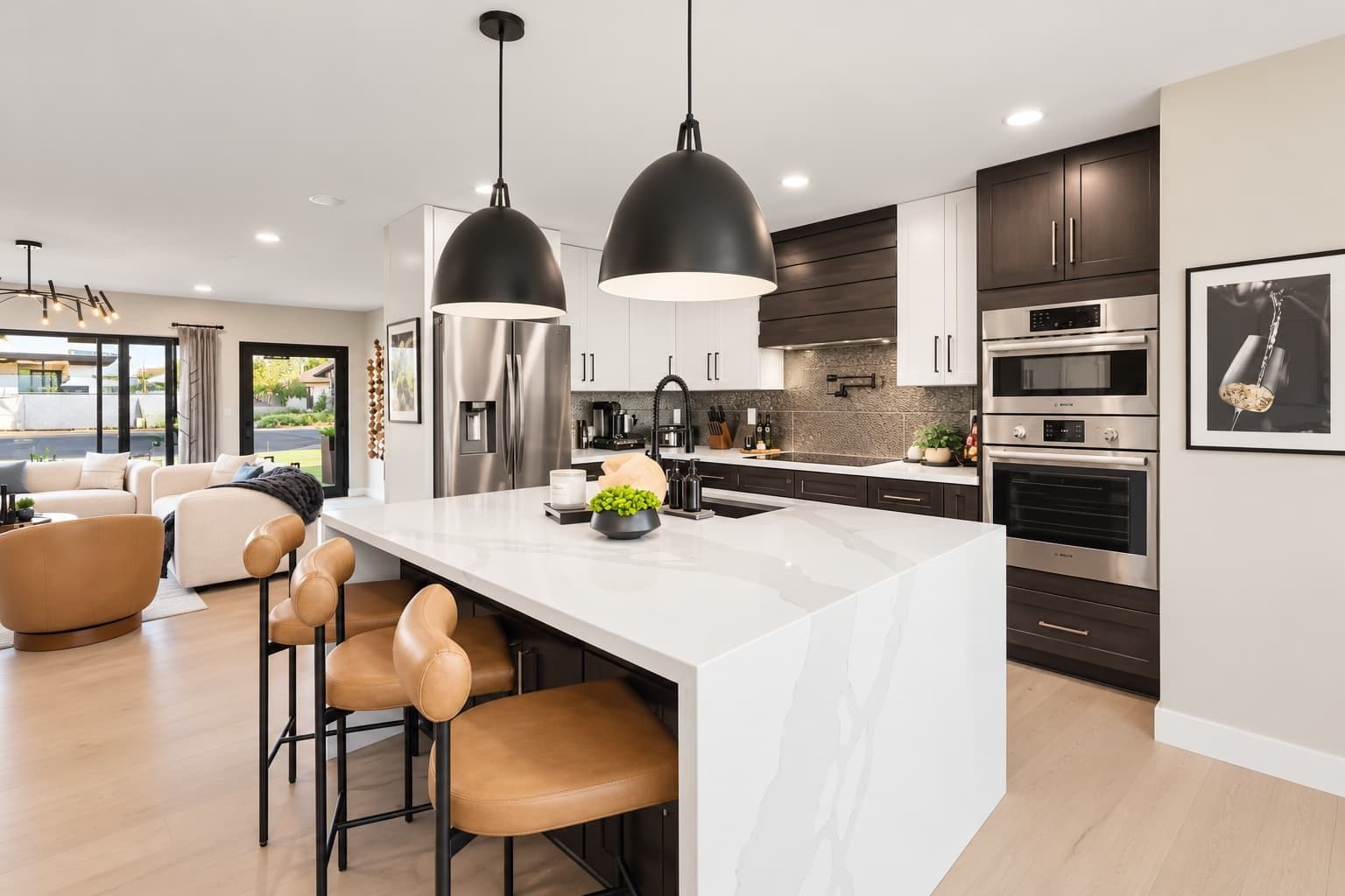 Une cuisine moderne dotée d’un grand îlot central, d’appareils électroménagers en acier inoxydable et de luminaires suspendus.