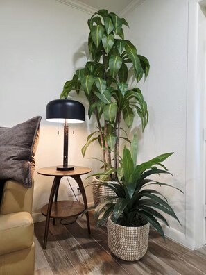 A room with a round wooden table, a floor lamp, a sofa, and two potted plants. - Premier Studio Private Laundry Parking Pool Patio (El Paso)