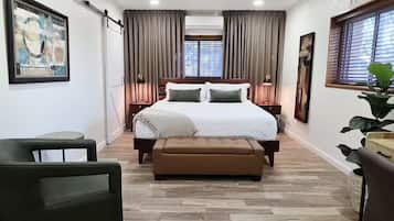 Een slaapkamer met een bed, een bankje, een stoel, een plafondventilator en een raam met gordijnen.