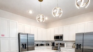 A modern kitchen with white cabinetry, stainless steel appliances, and pendant lighting. - Value Edge (Kissimmee)