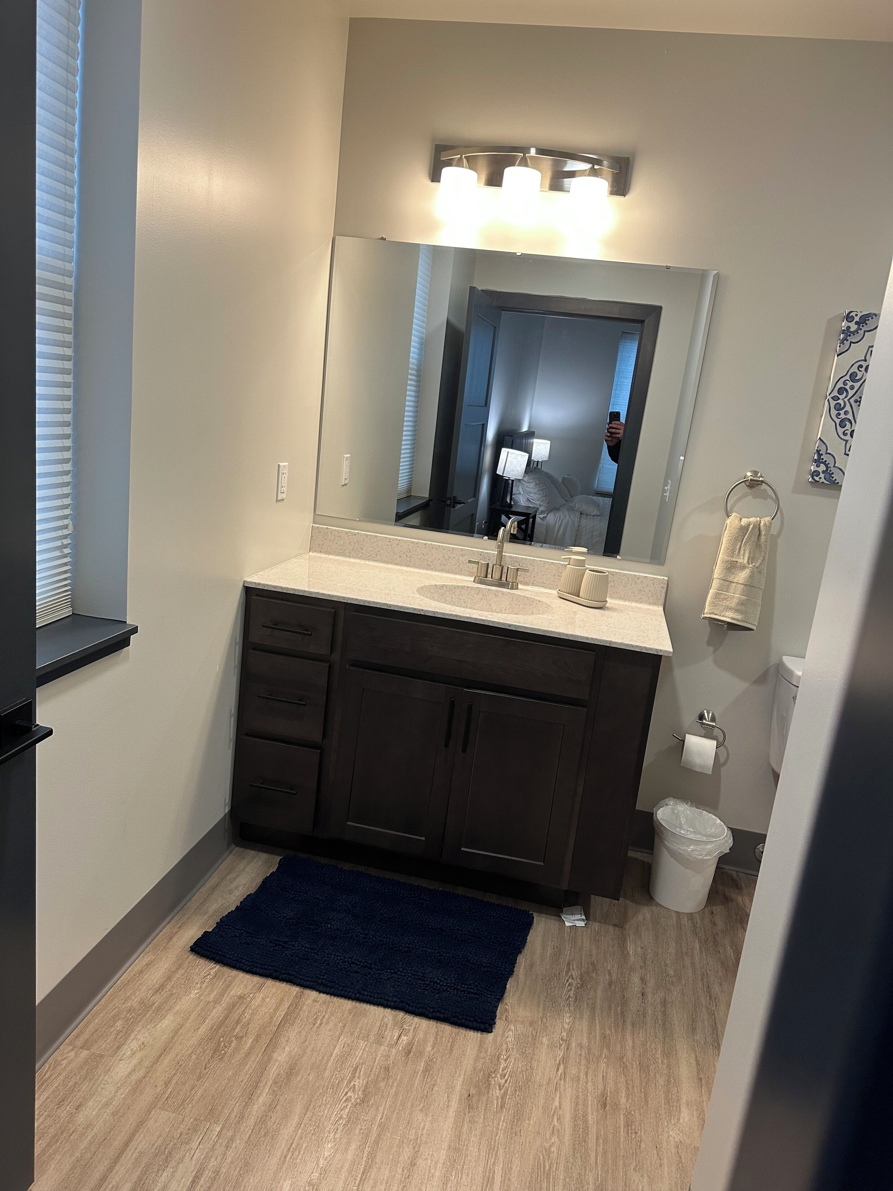 A bathroom with a dark wood vanity, a large mirror, a towel rack, and a trash can.