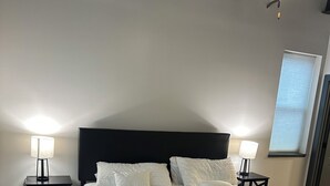 A bedroom with a large bed, two bedside tables, a ceiling fan, and a window with blinds. - Luxury King Suite Downtown Kalamazoo (Kalamazoo)
