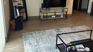 A modern living room with a flat-screen TV, a glass coffee table, and a patterned rug. - Luxury King Suite Downtown Kalamazoo (Kalamazoo)