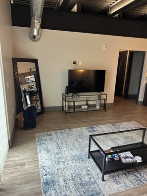 A modern living room with a flat-screen TV, a glass coffee table, and a patterned rug. - Luxury King Suite Downtown Kalamazoo (Kalamazoo)