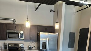 A modern kitchen with stainless steel appliances, a granite countertop, and wooden stools. - Luxury King Suite Downtown Kalamazoo (Kalamazoo)