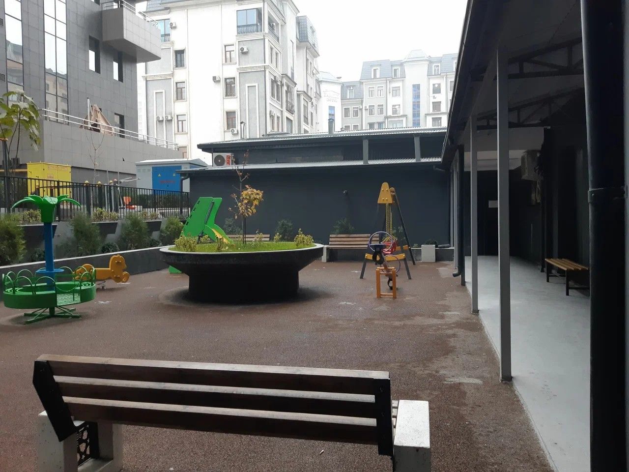 An outdoor area with a playground, benches, and a building in the background.