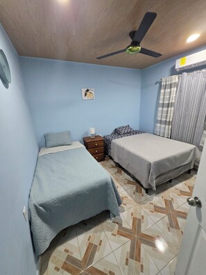A bedroom with two beds, a ceiling fan, a nightstand, and a wall-mounted air conditioner.