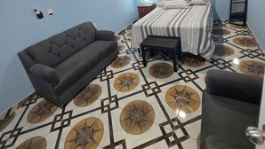 Ein Schlafzimmer mit einem Bett, einem Schlafsofa, einem kleinen Tisch, einem Deckenventilator und einem gemusterten Boden.