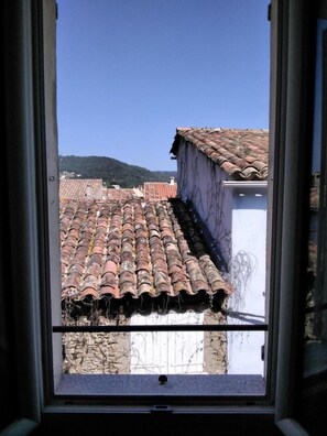 Blick aus dem Fenster auf terrakottafarbene Dächer, ein weißes Gebäude und eine Hügelkulisse im Hintergrund.
