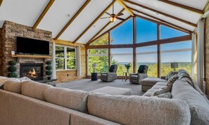 A spacious living room with a stone fireplace, comfortable seating, and large windows offering a view of the outdoors. - Cliffside Cabin, Stunning views and 100% privacy (West Decatur)