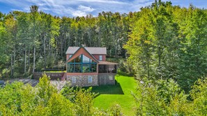 A modern house with a large glass window, surrounded by a lush green forest.