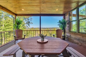 Eine Holzterrasse mit Tisch und Bänken, umgeben von Glasgeländern, mit Blick auf eine bewaldete Landschaft.