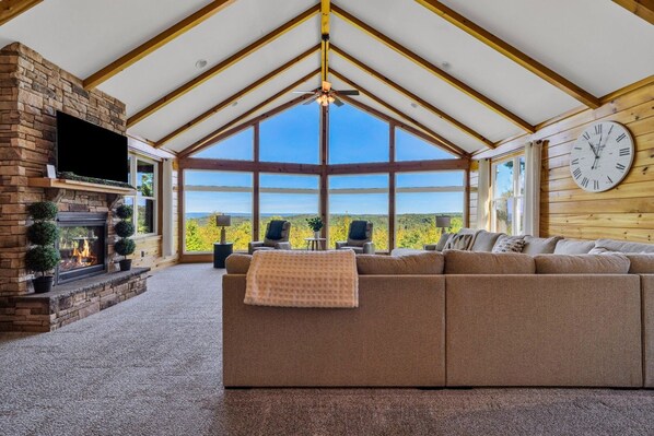 A spacious living room with a fireplace, a large sofa, and a view of the outdoors. - Cliffside Cabin, Stunning views and 100% privacy (West Decatur)