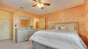 Ein Schlafzimmer mit Holzwandverkleidung, einem Bett, einem Schminktisch, einem Spiegel und einem Deckenventilator.