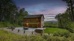 Eine zweigeschossige Blockhütte mit Terrasse, umgeben von einem Wald.