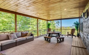 A covered outdoor seating area with a sofa, picnic table, and chairs, overlooking a forested landscape. - Cliffside Cabin, Stunning views and 100% privacy (West Decatur)