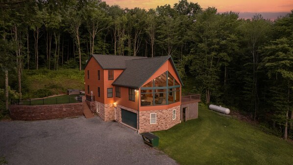A two-story log cabin with a garage, surrounded by a wooded area.