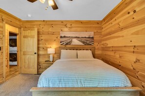 A wooden-paneled bedroom with a bed, a nightstand, a lamp, and a painting of a road.