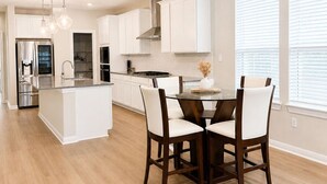 Una cocina moderna con armarios blancos, una isla central y un comedor con cuatro sillas.