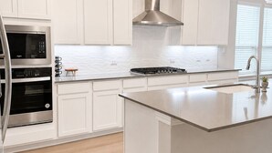 Una cocina moderna con armarios blancos, electrodomésticos de acero inoxidable, una isla central e iluminación colgante.