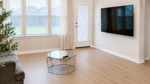 Un salón amplio con ventilador de techo, televisor grande y mesa de comedor.