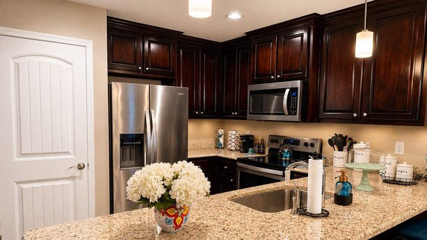 Una cocina con armarios de madera oscura, electrodomésticos de acero inoxidable, encimera de granito y un jarrón con flores.