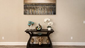 Una habitación con una pared color beige, una consola negra con objetos decorativos, y un cuadro abstracto grande encima.