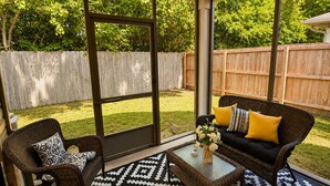 Un patio techado con muebles de mimbre, una mesa de centro de vidrio y una alfombra estampada.