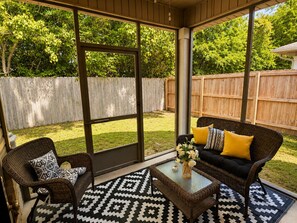 Eine überdachte Terrasse mit Korbmöbeln, einem Glastisch und einem gemusterten Teppich.