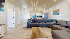 Un'ampia zona giorno con soffitto in legno, un divano spazioso, un tavolino da caffè e una cucina sullo sfondo.