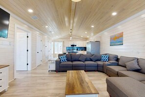 A spacious living area with a wooden ceiling, a large sofa set, a coffee table, and a kitchen in the background. - CL6 Shared Pool, Charcoal Grill, Old Town Port A (Port Aransas)