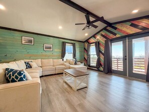 Ein geräumiges Wohnzimmer mit einem Ecksofa, einem Couchtisch und einem Deckenventilator.