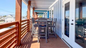 A covered outdoor balcony with wooden railings, a table with chairs, and a view of the surrounding area. - CL7 Shared Pool, Charcoal Grill, Old Town Port A (Port Aransas)