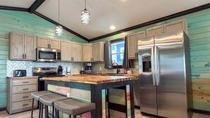 A kitchen with wooden cabinets, a stainless steel refrigerator, a microwave, and a coffee maker. - CL7 Shared Pool, Charcoal Grill, Old Town Port A (Port Aransas)