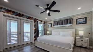 Une chambre à coucher avec un lit, un ventilateur de plafond, une table de chevet et une fenêtre avec des rideaux.