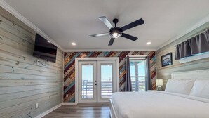 Une chambre avec un lit, un ventilateur de plafond et une vue sur l’extérieur, visible à travers la porte.