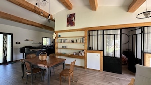 A dining area with a wooden table and chairs, a kitchen with a window, and a bookshelf.