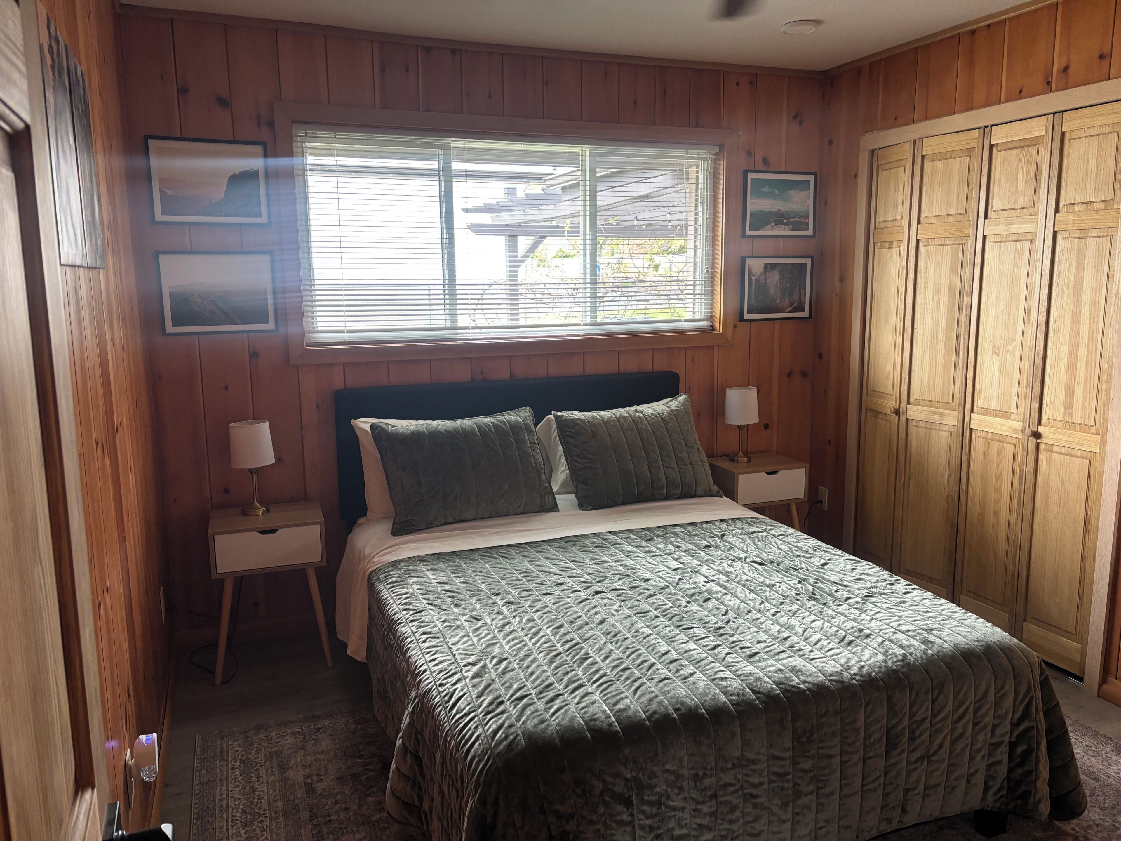 A wooden-paneled bedroom with a bed, two bedside tables, a window, and a wardrobe.