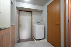 A small room with a wooden wardrobe, a white refrigerator, and a door leading to another room. - Dc Sakura Hotel - Namba Branch (Osaka)