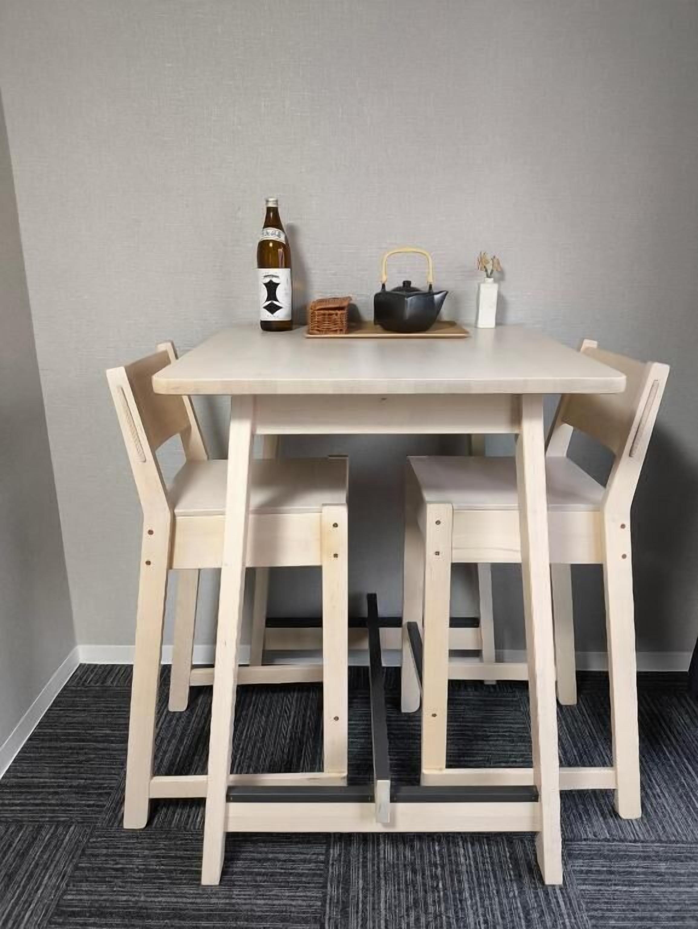 Una pequeña mesa de madera con dos sillas, una botella, un hervidor y una cesta.