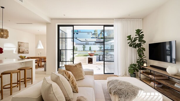 A modern living room with a sofa, TV, and a large window overlooking a garden. - Casa Bianca, Bondi IH (Bondi)