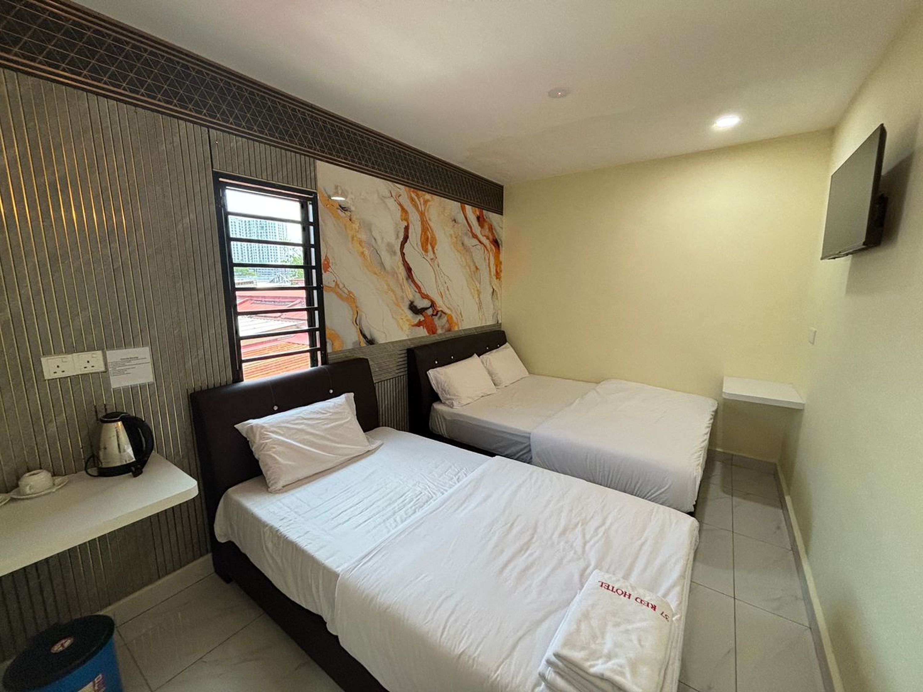 A hotel room with two beds, a small table, a kettle, and a TV mounted on the wall.