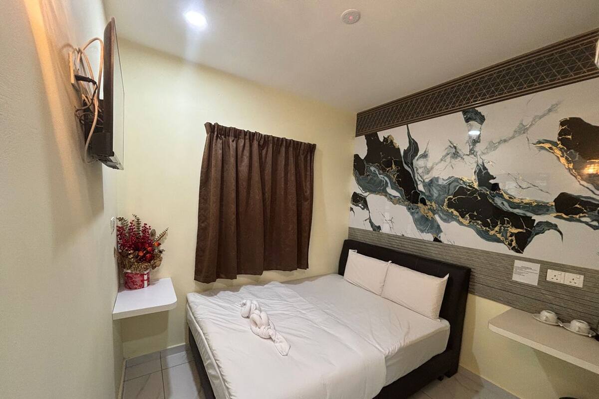 Habitación de hotel con cama, televisor montado en la pared, una mesita con un florero y un adorno en la pared.
