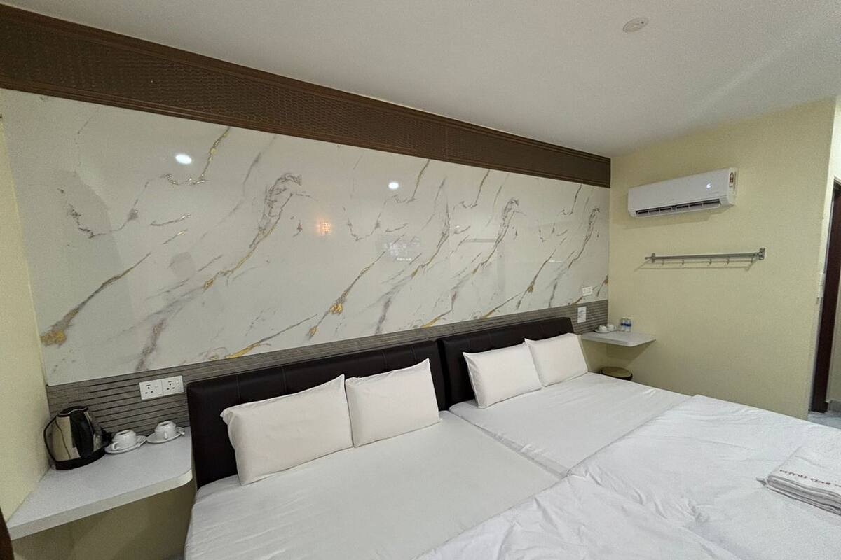 Habitación de hotel con una cama grande, cabecera de mármol, unidad de aire acondicionado, estante pequeño con artículos de aseo y mesita de noche.