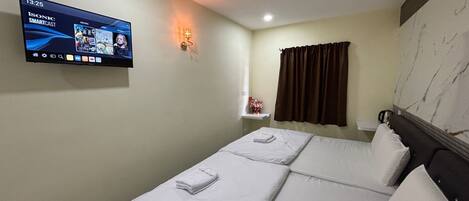 Quarto de hotel com duas camas, uma televisão de tela plana na parede, uma mesinha com um vaso de flores e uma janela com cortinas.
